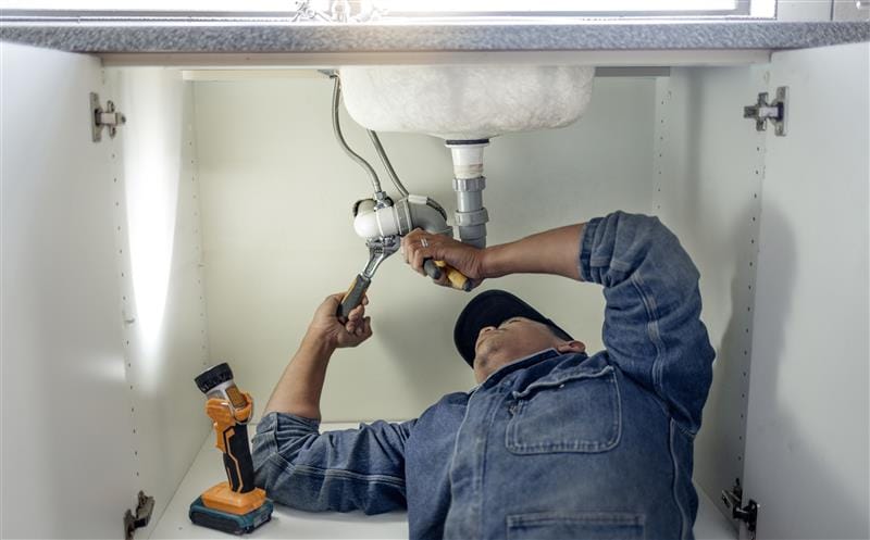 Plumber repairing pipes beneath a bathroom sink in Stuart