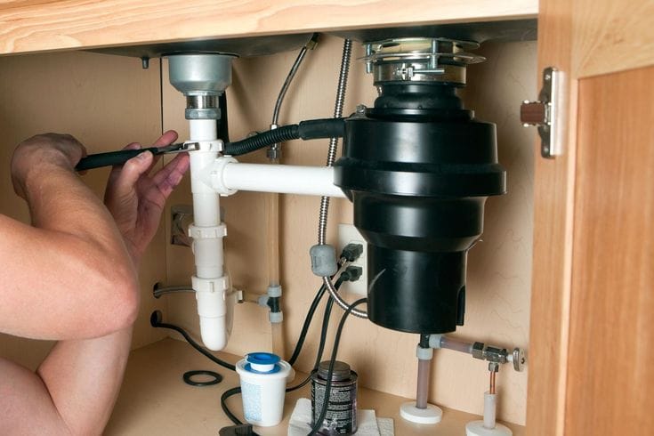 Plumber installing a garbage disposal beneath a kitchen sink in Stuart