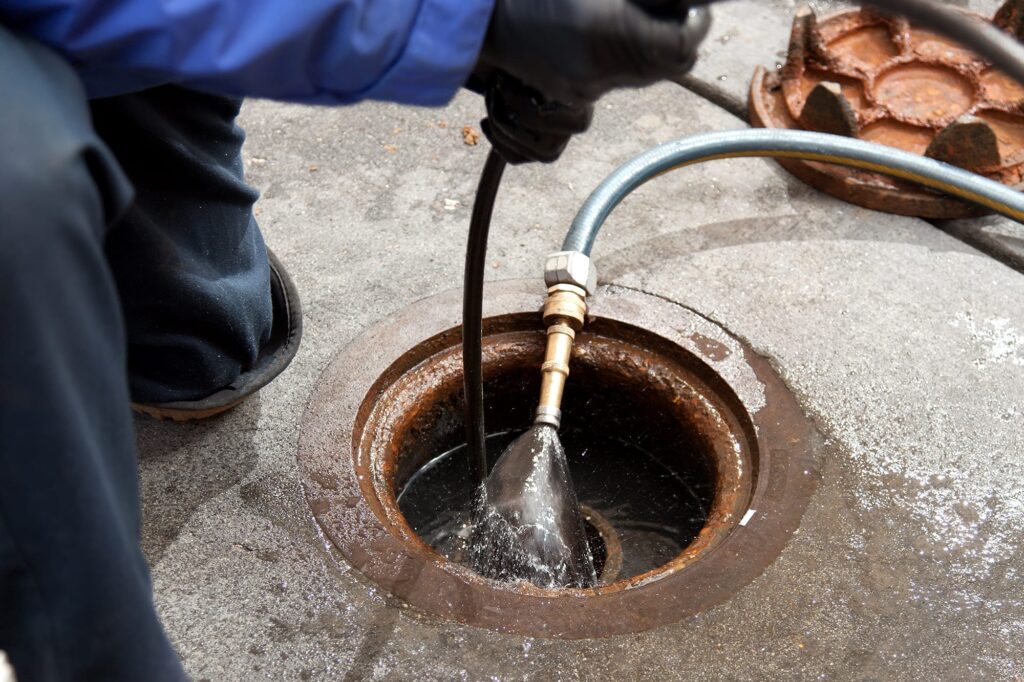 Plumber hydro jetting a sewer line through a manhole in Stuart