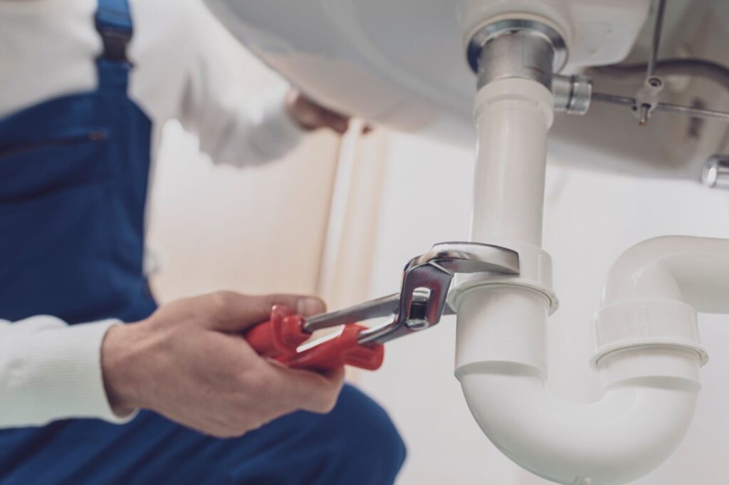 Plumber repairing a white drain pipe beneath a sink in Stuart